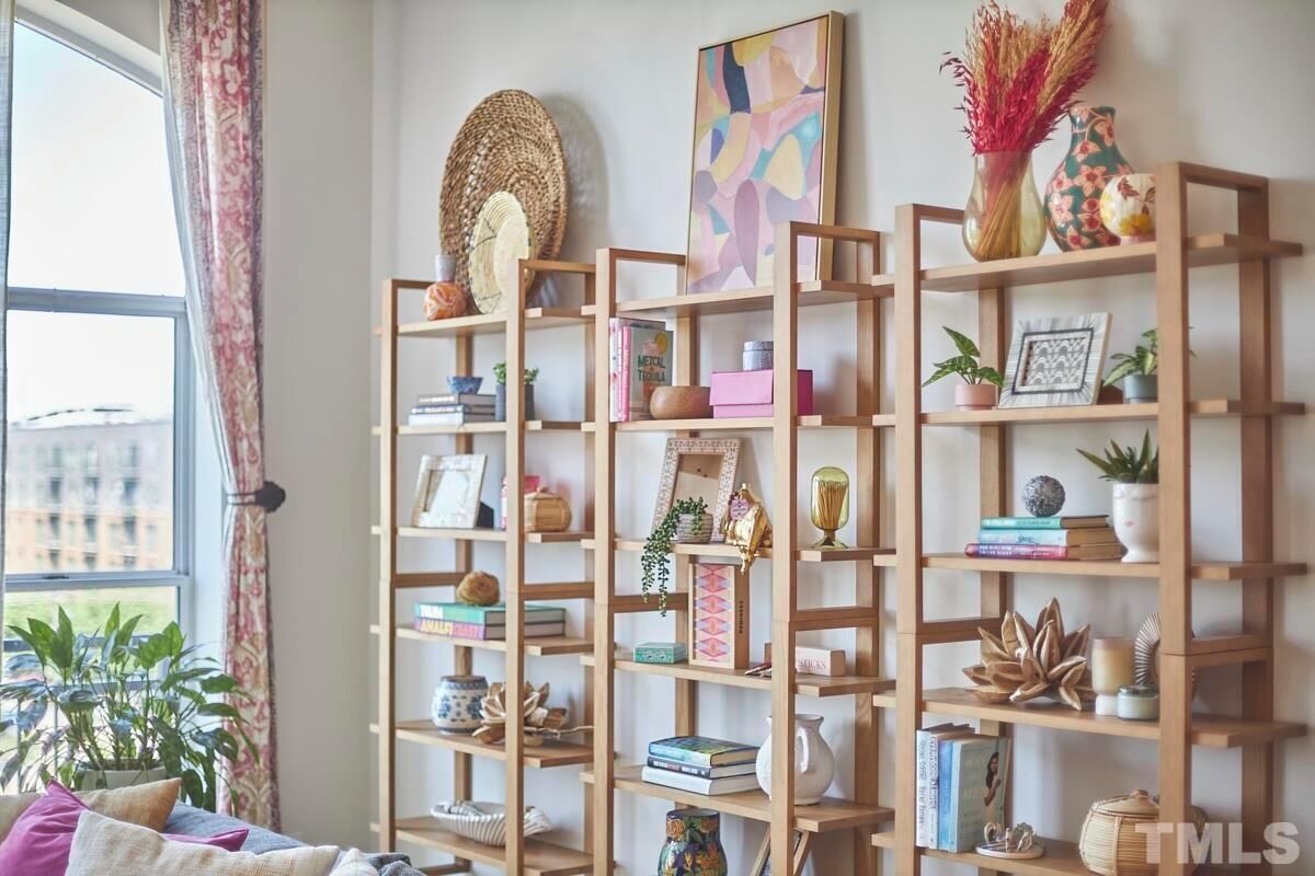 A room with a large window, a wooden bookshelf filled with books and decorative items, and a view of buildings outside.