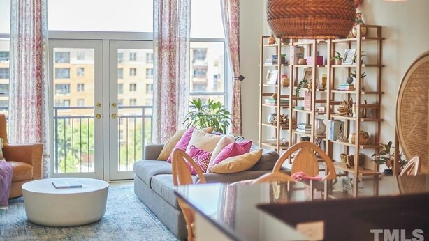 A living room with a sofa, chairs, a coffee table, a bookshelf, and a large window with curtains. - Luxe Downtown Penthouse! In the Heart of City w/Parking!! (Raleigh)