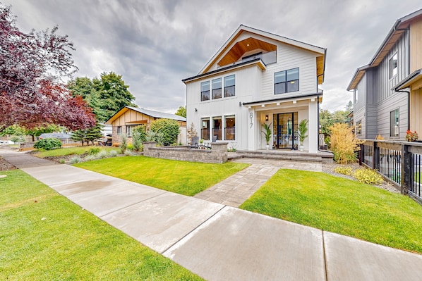 Stunning two-story home with a gabled roof and large windows, featuring a well-maintained lawn and paved driveway.