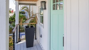 Un porche abrité avec un plafond en bois, une porte vert clair, un pot de fleurs noir et un paillasson.