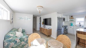 Un appartement moderne comprenant un salon, un coin repas, une cuisine et un couloir menant à une chambre.