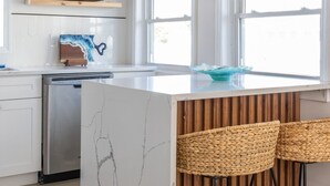 Une cuisine moderne dotée d’un îlot en marbre, de tabourets de bar en bois et de luminaires suspendus.