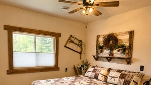 Quarto com uma cama grande, ventilador de teto, janela e prateleira na parede com objetos decorativos.