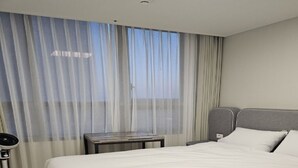 Una camera d'albergo con un letto grande, un comodino con una lampada e una finestra con tende leggere.