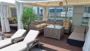Una terrazza panoramica con arredi in vimini, un tavolo in vetro e vista sulla città.