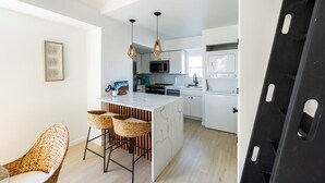 Cozinha moderna com armários brancos, uma ilha central e um espaço de jantar com cadeiras de vime.