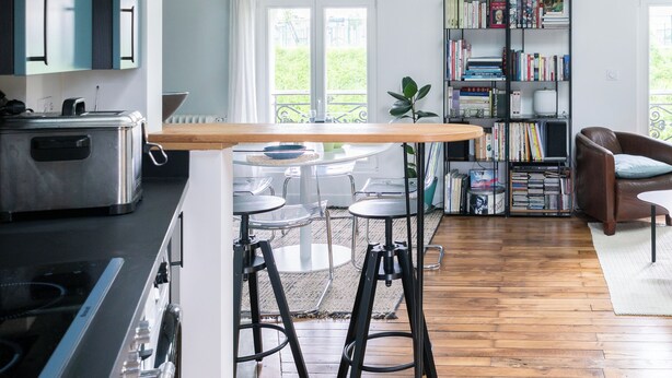 A modern kitchen with a wooden island, pendant lights, and a bookshelf in the living area. - Attractive architect-designed apartmenteur 3 rooms 10 mn from Paris Montparnasse (Malakoff)