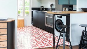A modern kitchen with wooden flooring, a washing machine, and a dining area with stools. - Attractive architect-designed apartmenteur 3 rooms 10 mn from Paris Montparnasse (Malakoff)