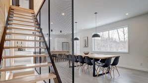 A modern interior with a wooden staircase, a dining area with a table and chairs, and large windows. - In nature - Spa - Blizzard (Bolton-Est)