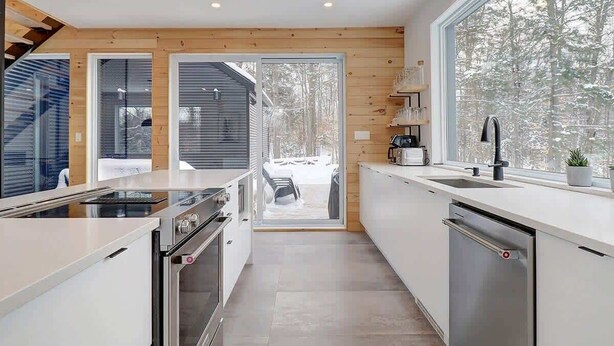 A modern kitchen with a large window, wooden walls, and a view of a snowy landscape. - In nature - Spa - Blizzard (Bolton-Est)