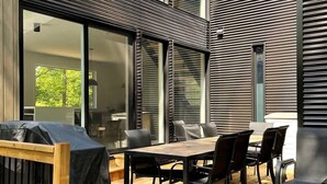 A modern outdoor patio with a wooden deck, a dining table with chairs, and a covered grill area. - In nature - Spa - Blizzard (Bolton-Est)