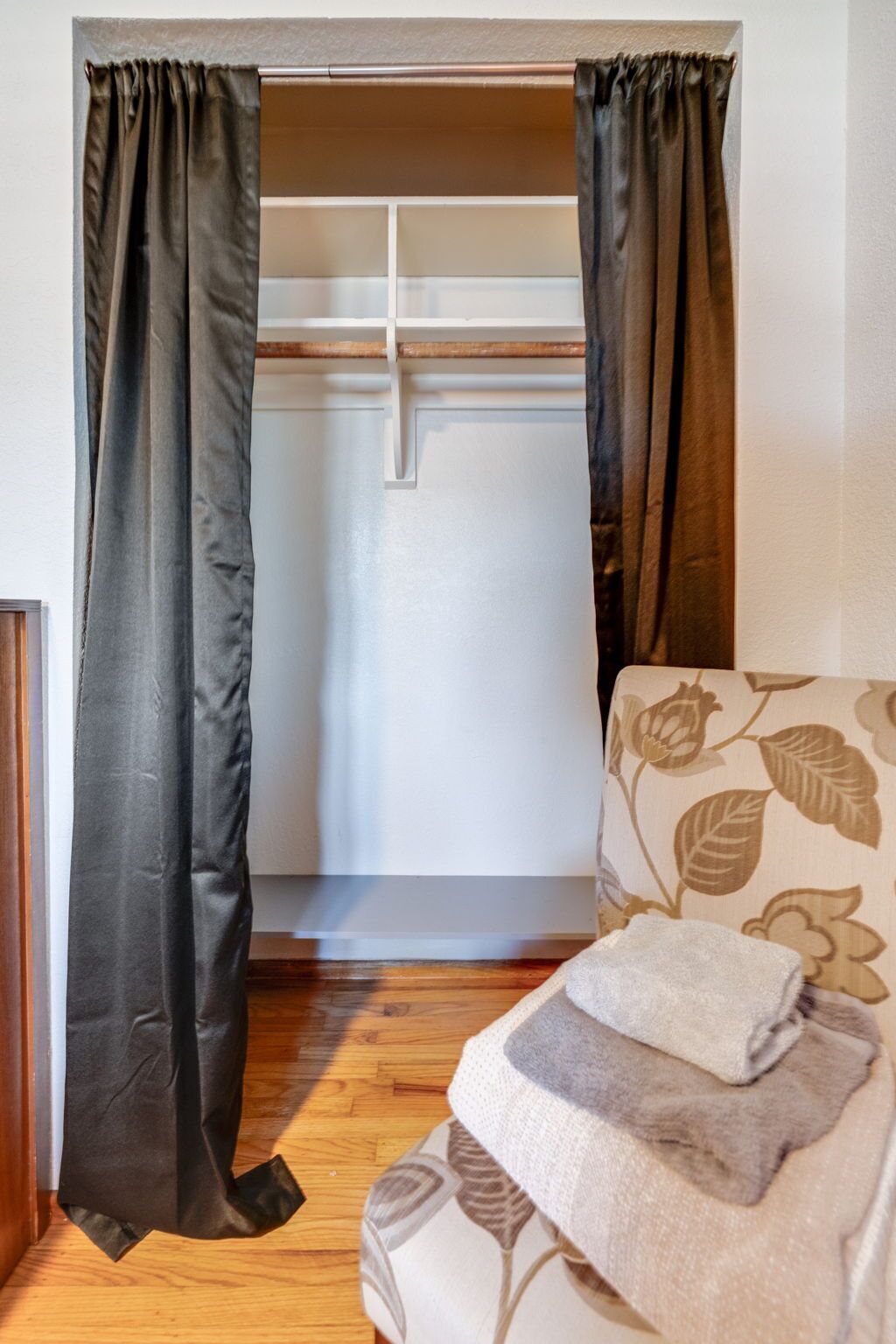 A room with a bed, a wooden floor, a white wall, and a wardrobe with a mirror.