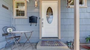 Una porta d'ingresso con un pannello di vetro decorativo, un tavolino con una sedia e un tappetino di benvenuto.