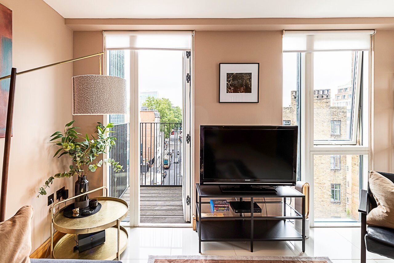 A modern living room with a large flat-screen TV, a round coffee table, a potted plant, and a view of the city through large windows.