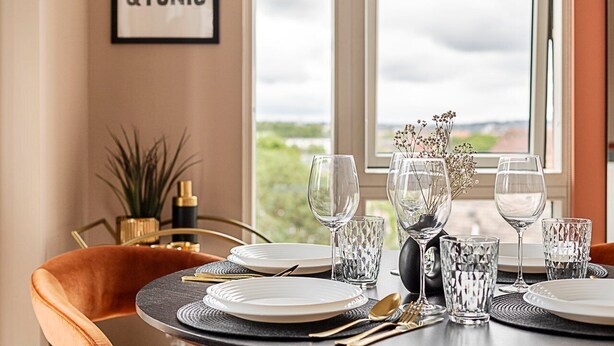 A dining table set with plates, glasses, and cutlery, a vase with flowers, and a framed sign on the wall.