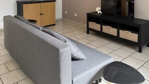Ein modernes Wohnzimmer mit einem grauen Sofa, einem Holzschrank, einer schwarzen Unterhaltungsecke und einem Fernseher.