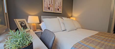A neatly arranged hotel room with a bed, bedside tables, a lamp, a framed picture, and a potted plant.