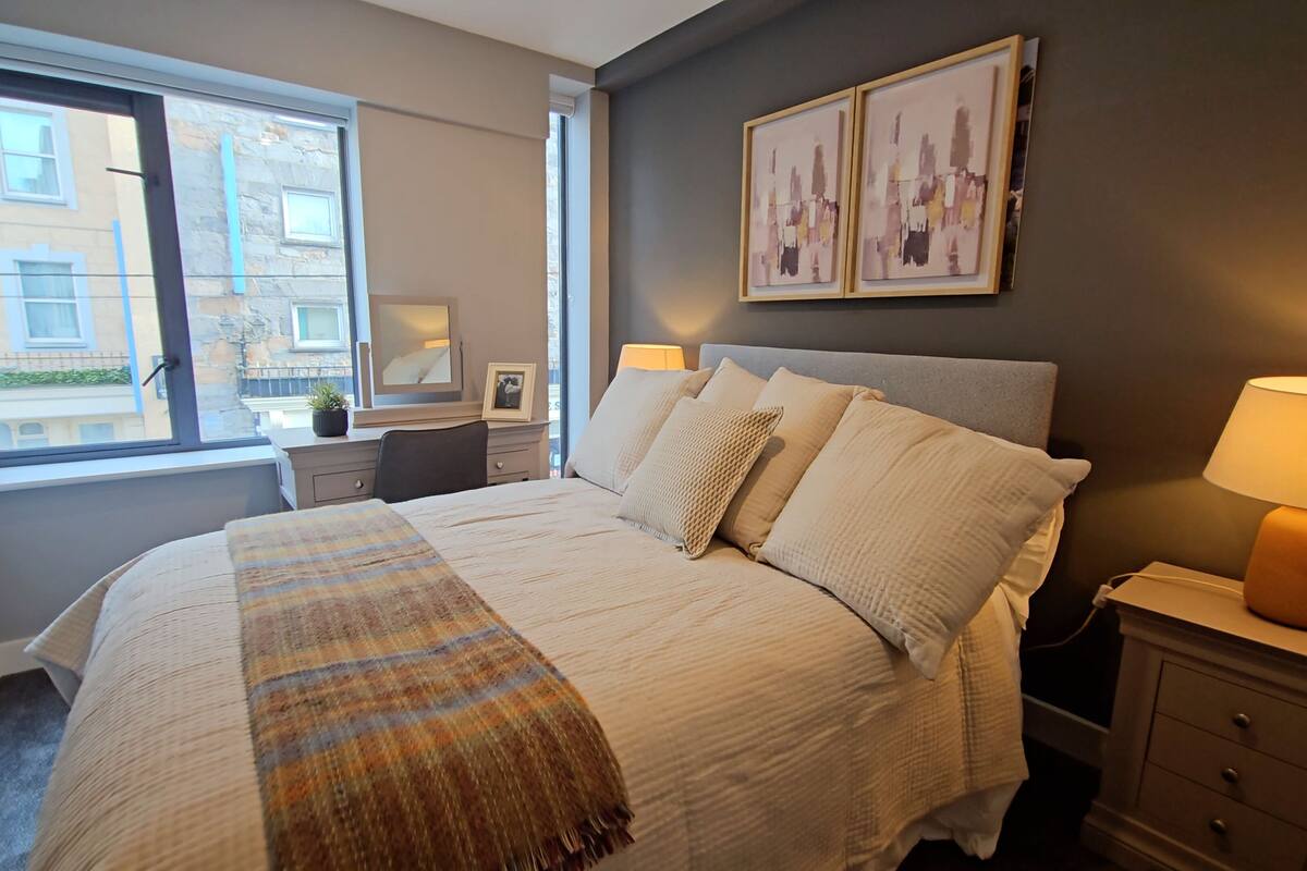 Une chambre à coucher bien rangée, avec un grand lit, des tables de chevet, une lampe et des œuvres d’art encadrées accrochées au mur.