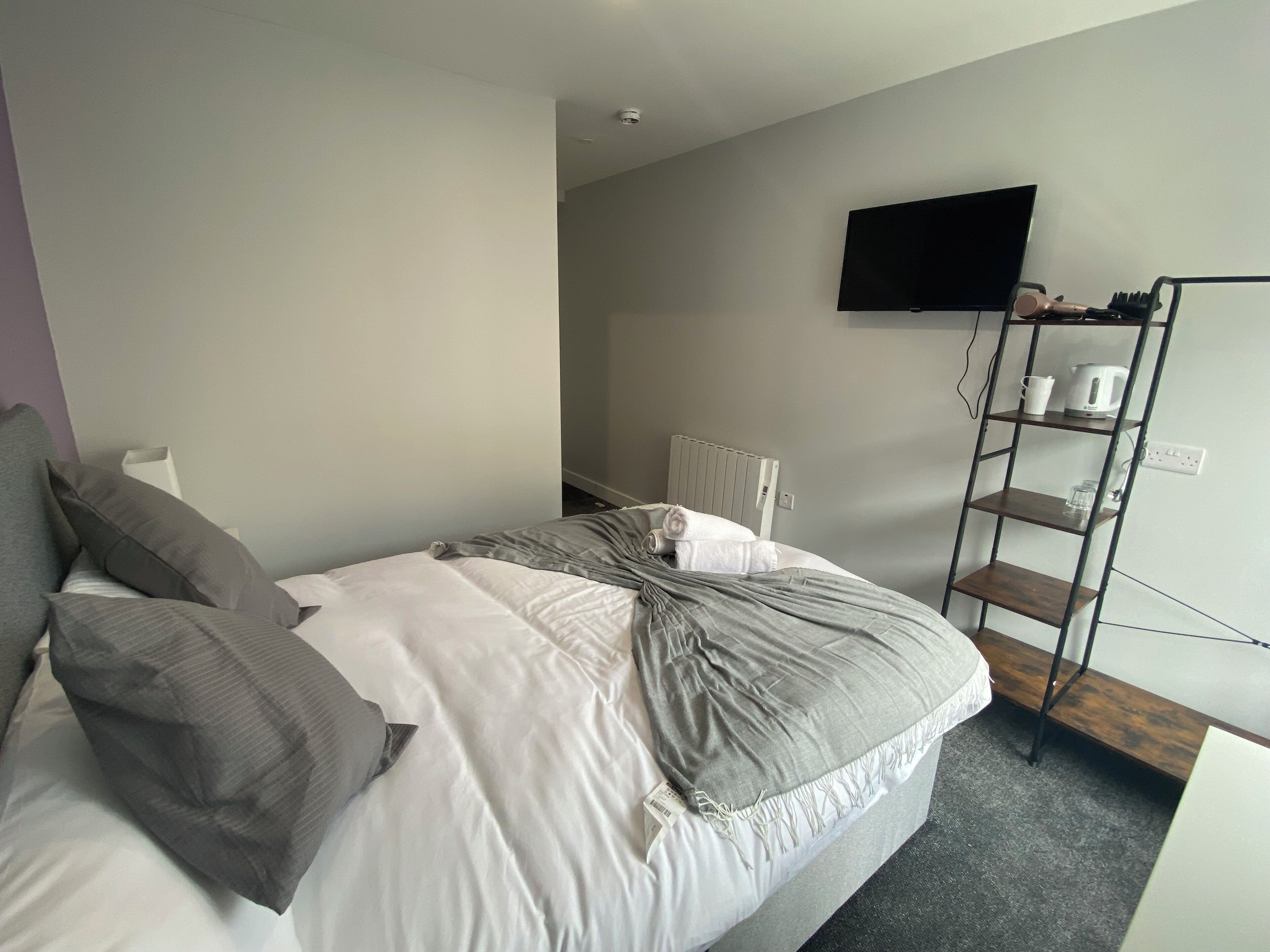 A bedroom with a bed, a TV mounted on the wall, and a shelf with items.