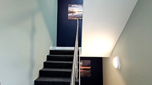 Un escalier avec une rampe, un tableau accroché au mur et un luminaire fixé au mur.
