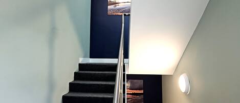 Una escalera con barandilla, un cuadro colgado en la pared y una lámpara de pared.