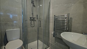 Une salle de bain moderne dotée d’une douche à parois de verre, de toilettes et d’un lavabo avec un porte-serviettes chromé.