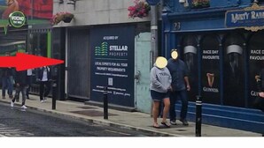 Une vue de rue avec une devanture de magasin faisant la publicité de services immobiliers, une pharmacie bien visible et un événement organisé à l’occasion d’une course.