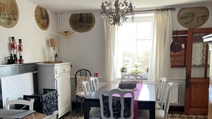 A dining area with a table set for four, surrounded by white chairs. A chandelier hangs from the ceiling, and the room features patterned tile flooring.