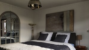 A bedroom with a large bed, a floor lamp, a painting on the wall, and a window with a view.