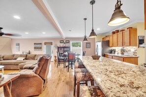 A spacious living room with a large brown leather sofa, a dining area with a long table and chairs, and a kitchen with wooden cabinets and a marble countertop. - Cozy Getaway, Grill, Spacious by Zen Living (Waxhaw)