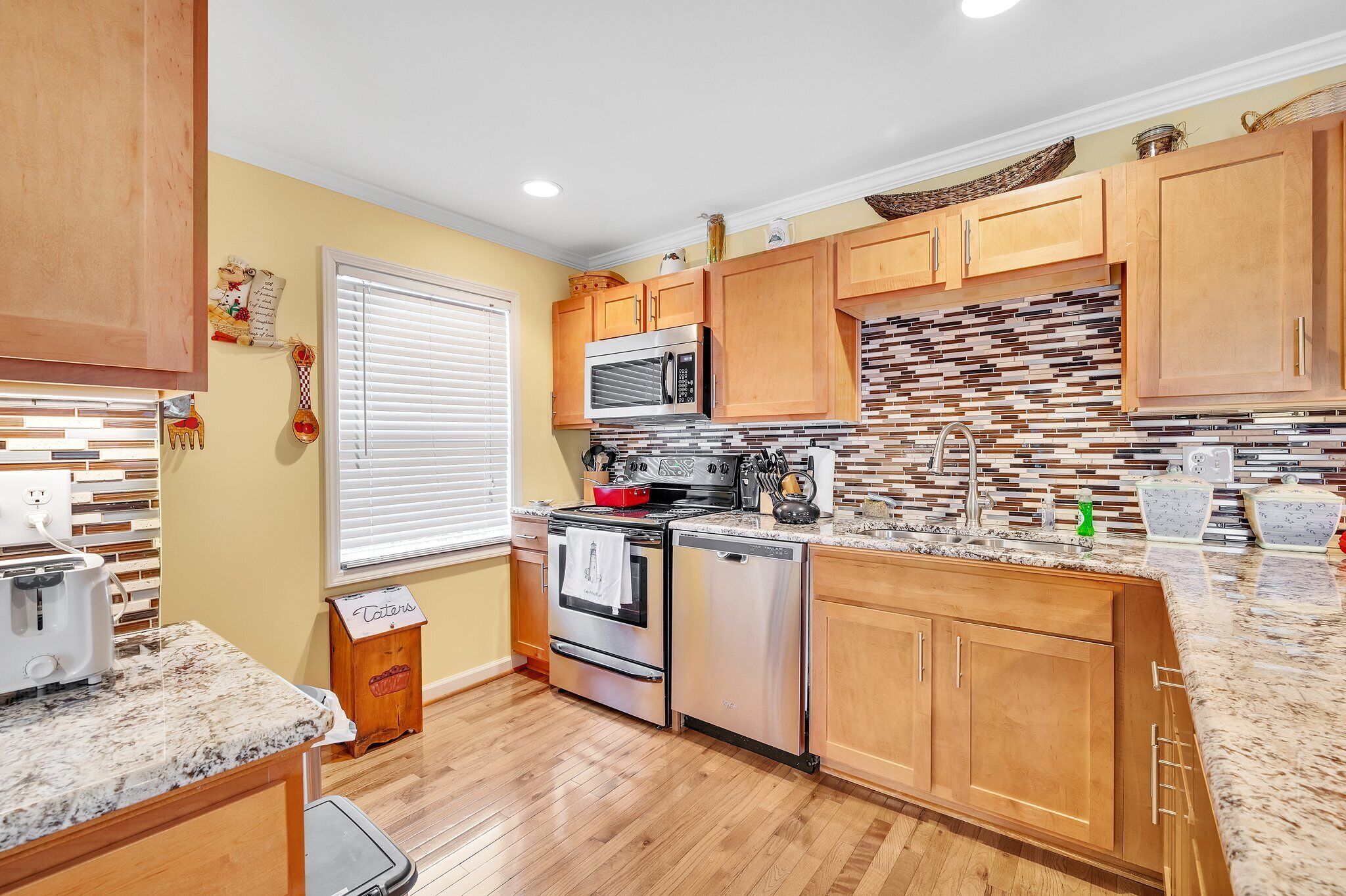 A kitchen with wooden cabinets, a stainless steel stove, a microwave, and a tiled backsplash.