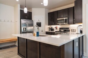 A modern kitchen with dark cabinets, stainless steel appliances, a large island with a sink, and pendant lighting. - Clearwater Lofts #302, Building 3 By Summit County Mountain Retreats (Keystone)
