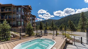 A wooden deck with a hot tub, a fenced area, and a view of a mountain and forest. - Clearwater Lofts #302, Building 3 By Summit County Mountain Retreats (Keystone)