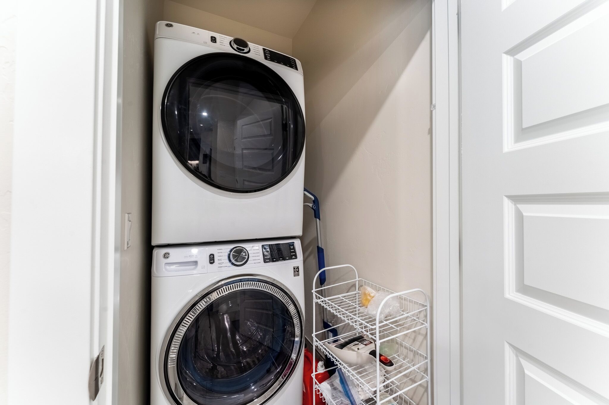 A laundry room with two stacked front-loading washing machines and a metal laundry basket.