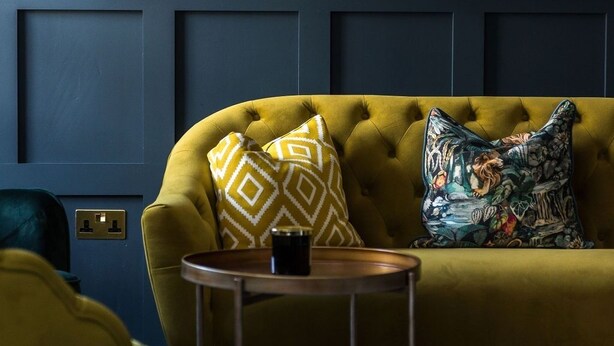 A room with a mustard yellow sofa, a round mirror with a gold frame, and a small round table with a black object on it. - Boutique Castle View 3 Bed, 1 Bath Apartment

​ (Edinburgh)