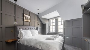 A bedroom with a large bed, a wooden nightstand, a pendant light, a framed picture on the wall, and a skylight. - Boutique Castle View 3 Bed, 1 Bath Apartment

​ (Edinburgh)
