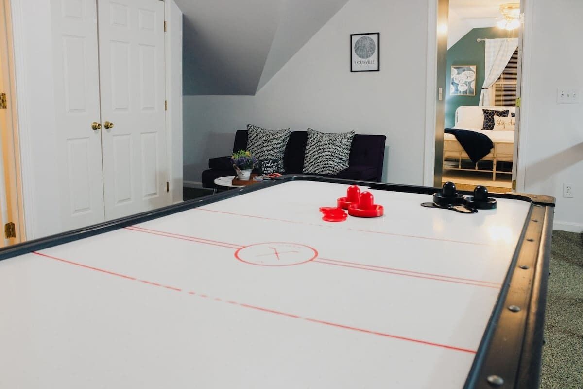 Une pièce comprenant une table de jeu de palet, un canapé avec des coussins à motifs et un tableau encadré accroché au mur.