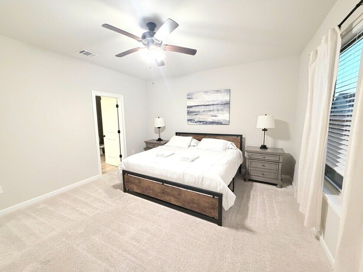 A bedroom with a bed, nightstands, a ceiling fan, and a window with curtains.