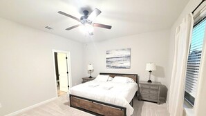 A bedroom with a bed, nightstands, a ceiling fan, and a window with curtains. - Purple Paws Pad for LSU Tigers on the Go -  CL5610 (Baton Rouge)