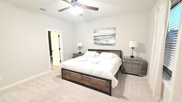 A bedroom with a bed, nightstands, a ceiling fan, and a window with curtains.