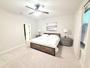 A bedroom with a bed, nightstands, a ceiling fan, and a window with curtains.