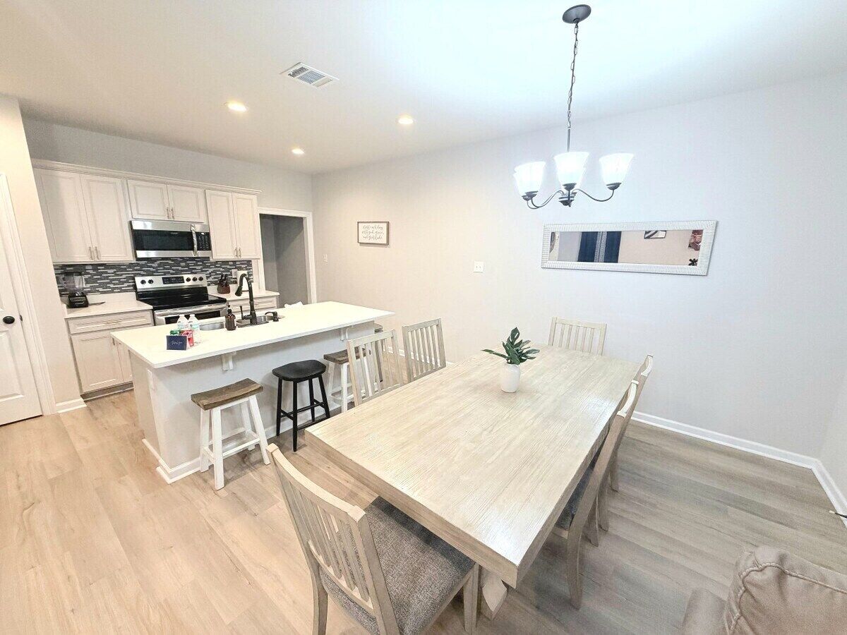 A modern kitchen with white cabinetry, a central island, and a dining area with a wooden table and chairs.