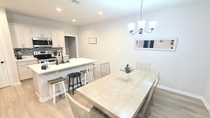 A modern kitchen with white cabinetry, a central island, and a dining area with a wooden table and chairs. - Purple Paws Pad for LSU Tigers on the Go -  CL5610 (Baton Rouge)