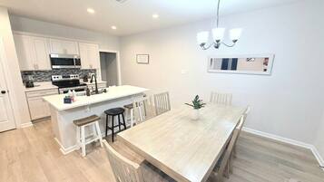 A modern kitchen with white cabinetry, a central island, and a dining area with a wooden table and chairs.