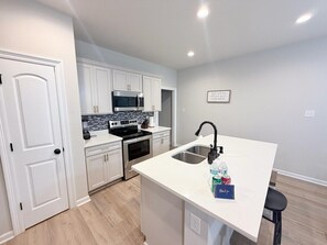 A modern kitchen with white cabinetry, a built-in microwave, and a stainless steel sink.