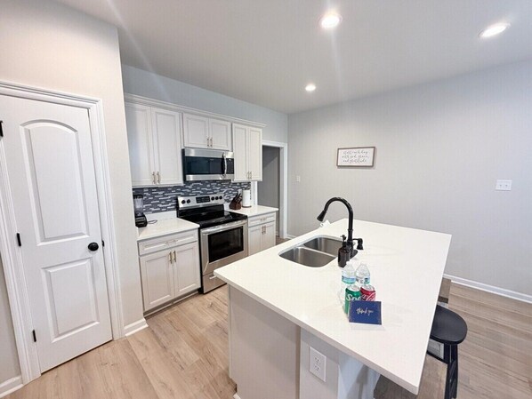 A modern kitchen with white cabinetry, a built-in microwave, and a stainless steel sink.