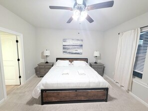 A bedroom with a bed, nightstands, a ceiling fan, and a window with curtains.