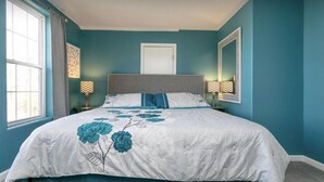 Een slaapkamer met een groot bed, twee nachtkastjes, een raam met gordijnen en een deur.