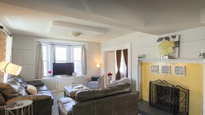 Een woonkamer met leren banken, een televisie, een open haard en een geel accentmuur.