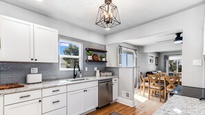 A modern kitchen with white cabinets, a granite countertop, and a backsplash. There is a dining area with a table and chairs, and a ceiling fan. - Experience Cheyenne in a cozy home, close to Downtown, Medical Center and CFD.  (Cheyenne)